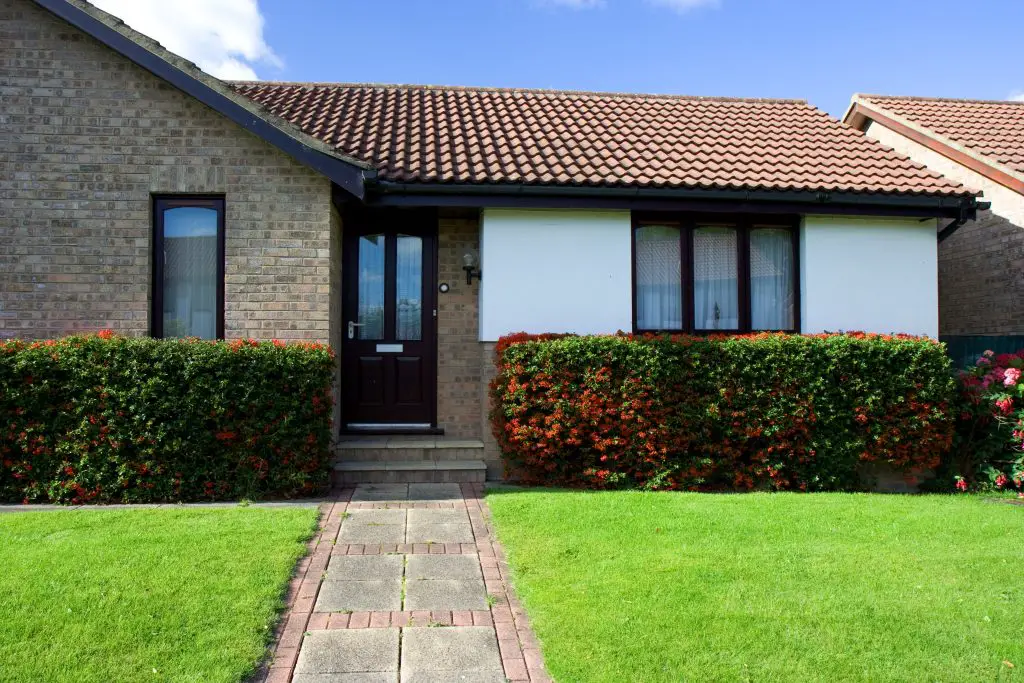 Brick bungalow with hedges and green lawn.