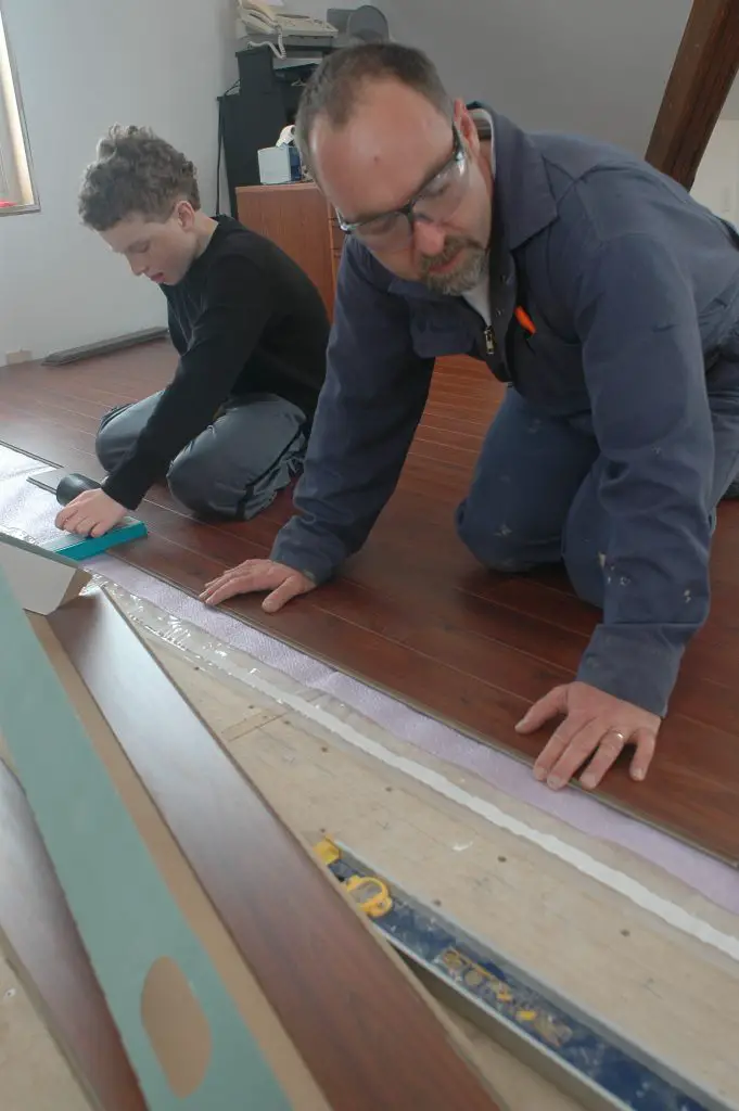 Two people installing laminate flooring together.