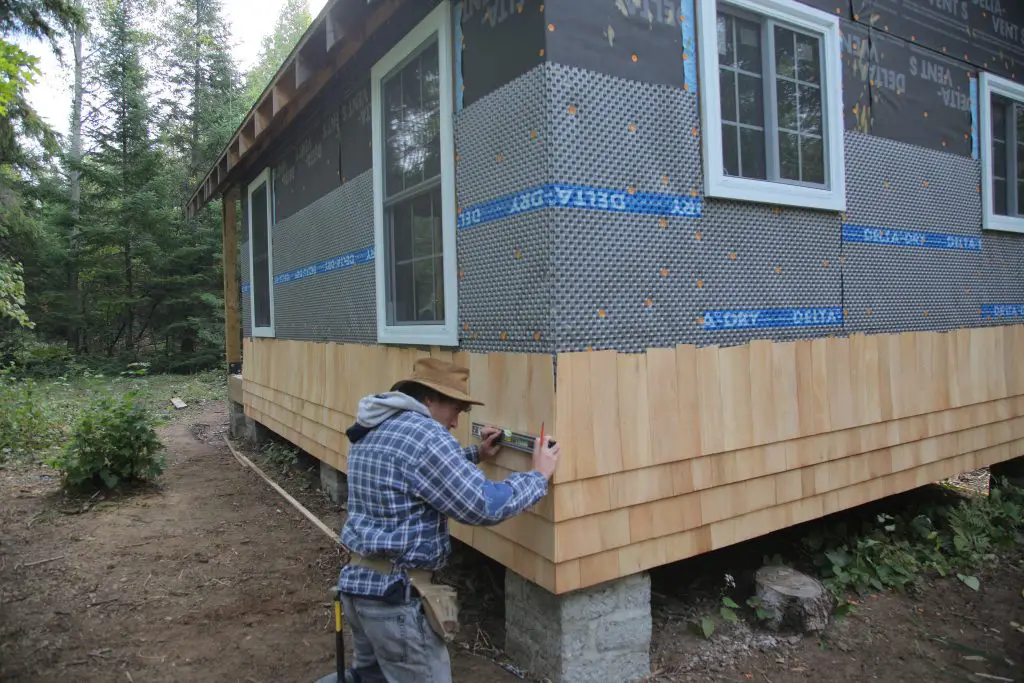 Person installing siding on house in forest.