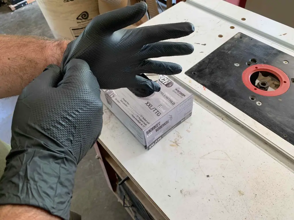 Person putting on black gloves near workbench.