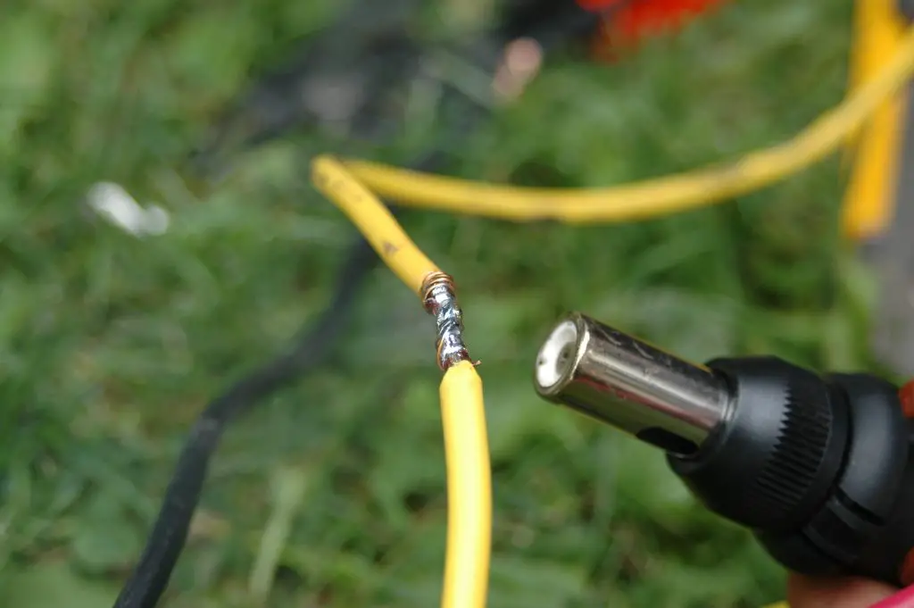 Soldering yellow wires outdoors with heat gun.