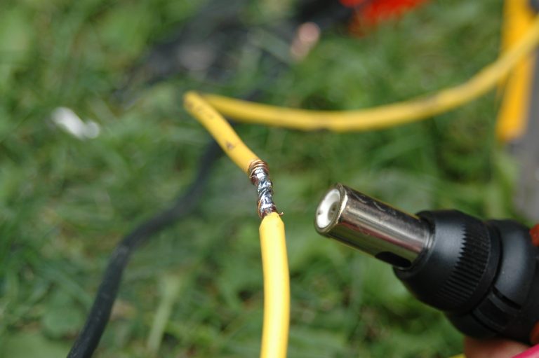 Soldering yellow wires outdoors with heat gun.