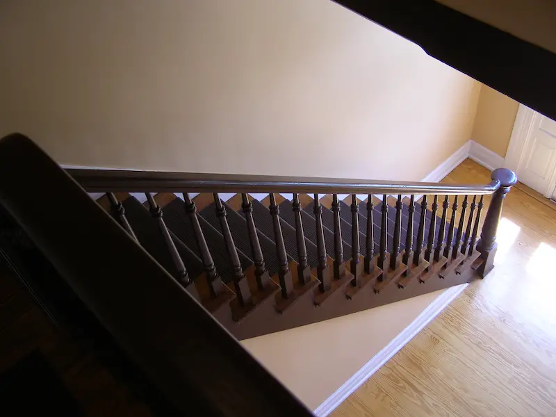 Wooden staircase with dark balusters and light walls.