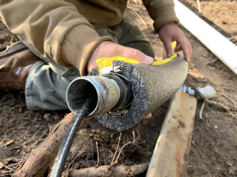 Person measuring insulated pipe outdoors with tape measure.