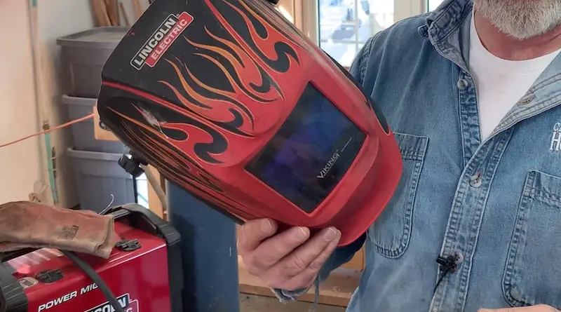 Man holding welding helmet in workshop.