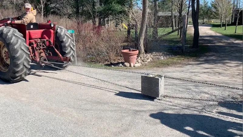 Tractor towing a heavy concrete block with chains.