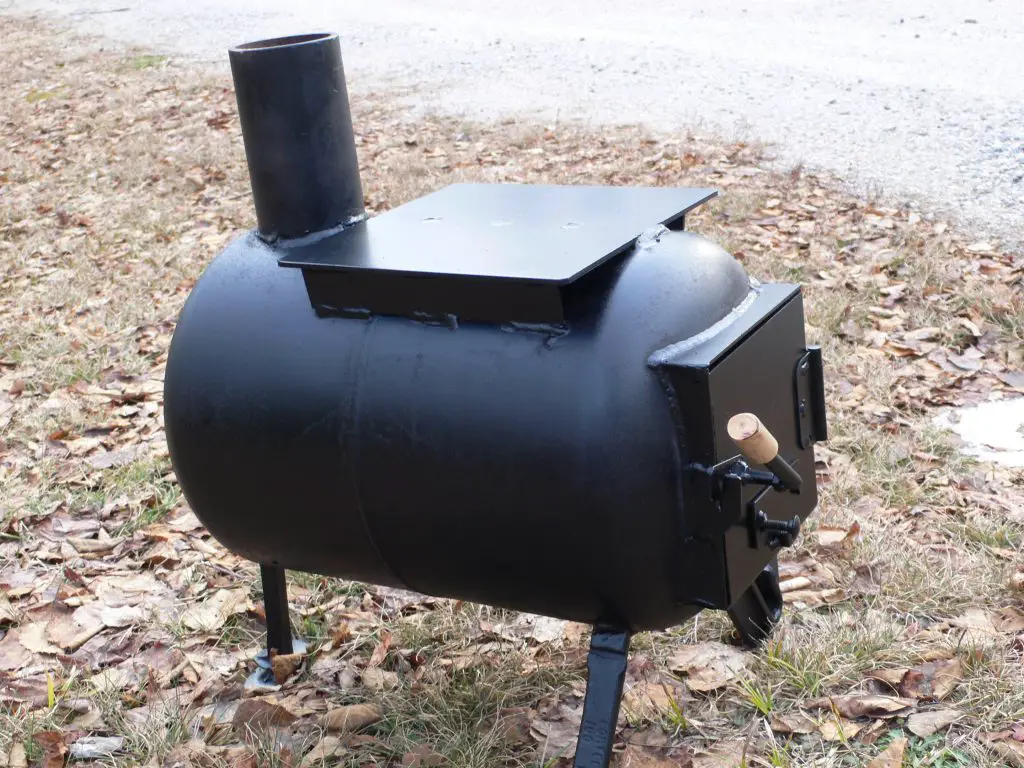 Portable black wood stove on leaves outside.