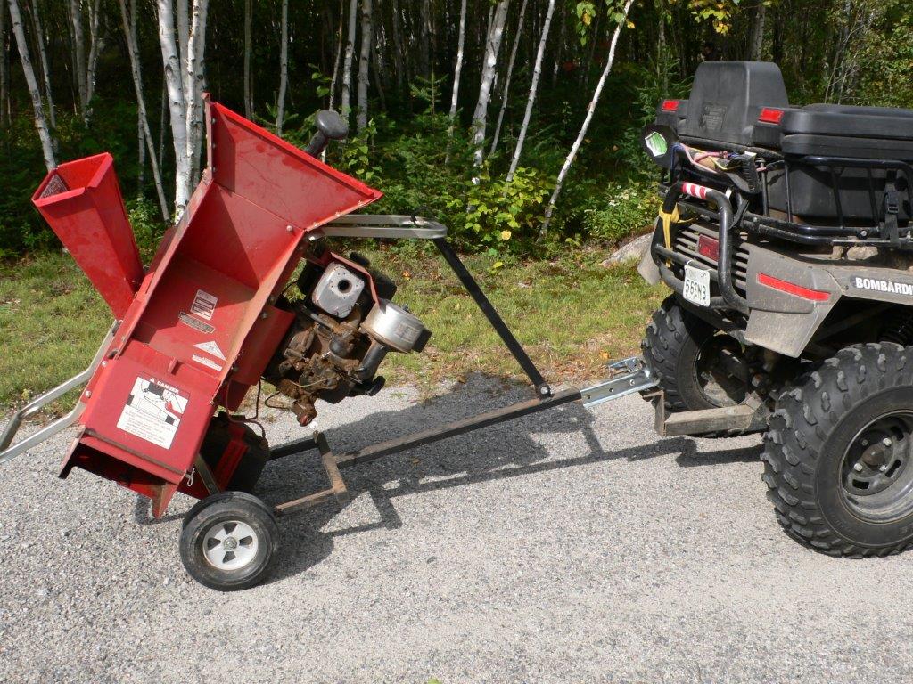 ATV towing red wood chipper on gravel path.