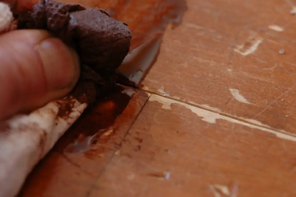 This close-up images shows dark brown stain being rubbed into a worn pine floor before recoating with urethane. This is much easier than sanding back to bare wood, and the results look amazing.