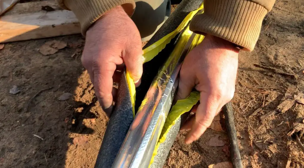 Hands wrapping pipe with insulation outdoors.