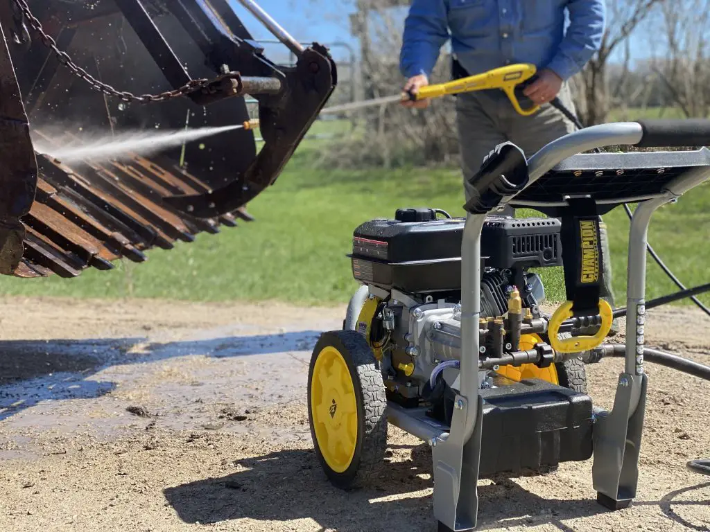 Person power washes an excavator bucket outdoors.