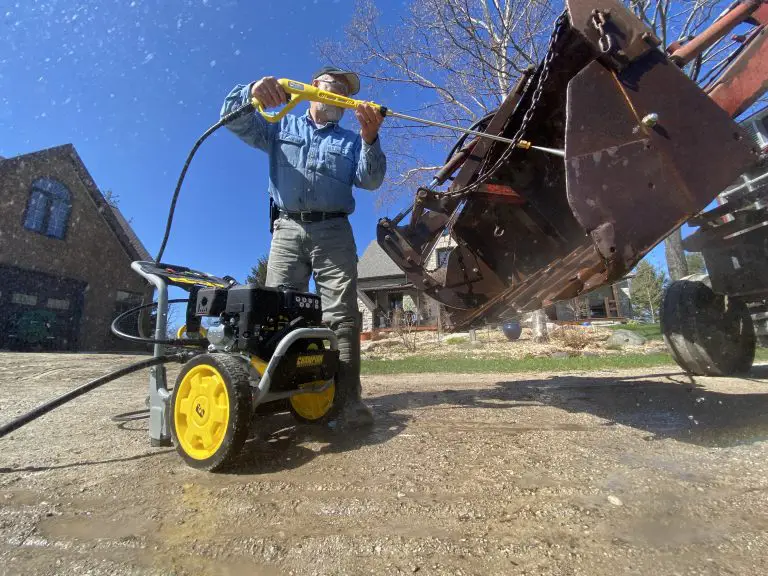Person using pressure washer on equipment outdoors.