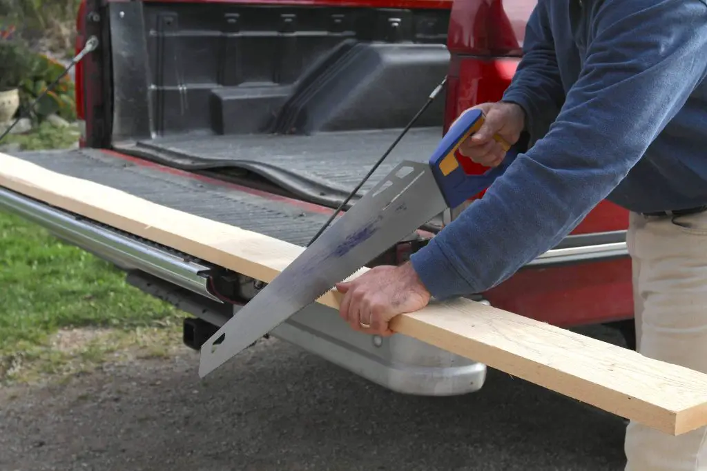 Person sawing wood on truck tailgate.