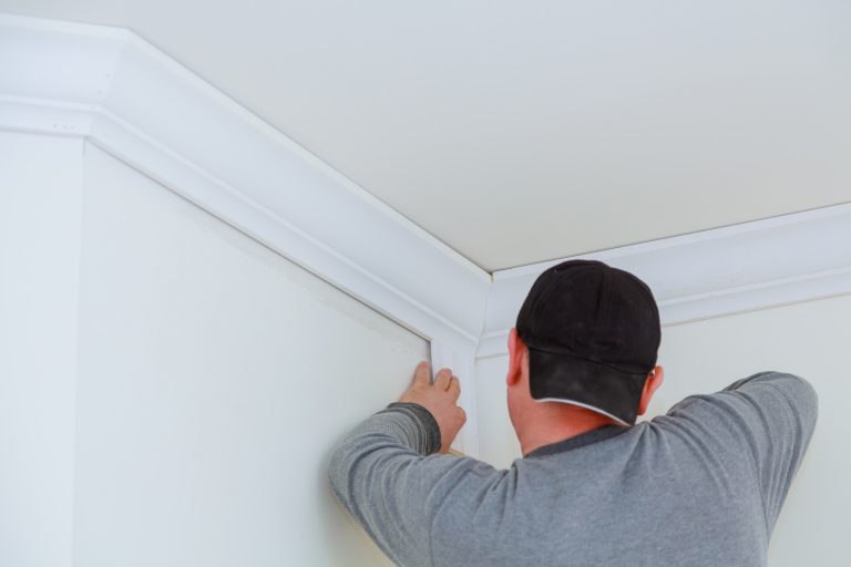 Worker installing crown moulding on ceiling corner.