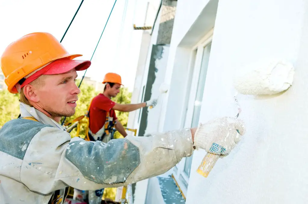 Construction workers painting building exterior white.