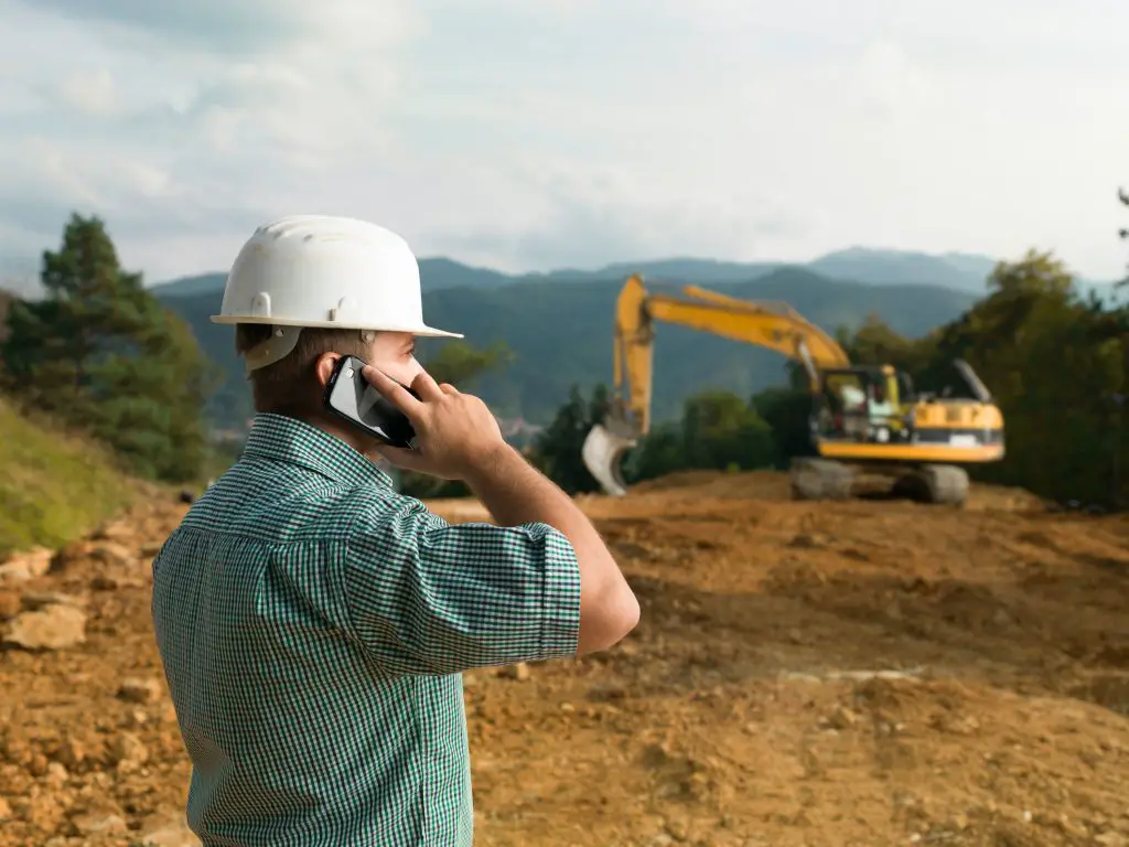 Construction worker on site with excavator in background.