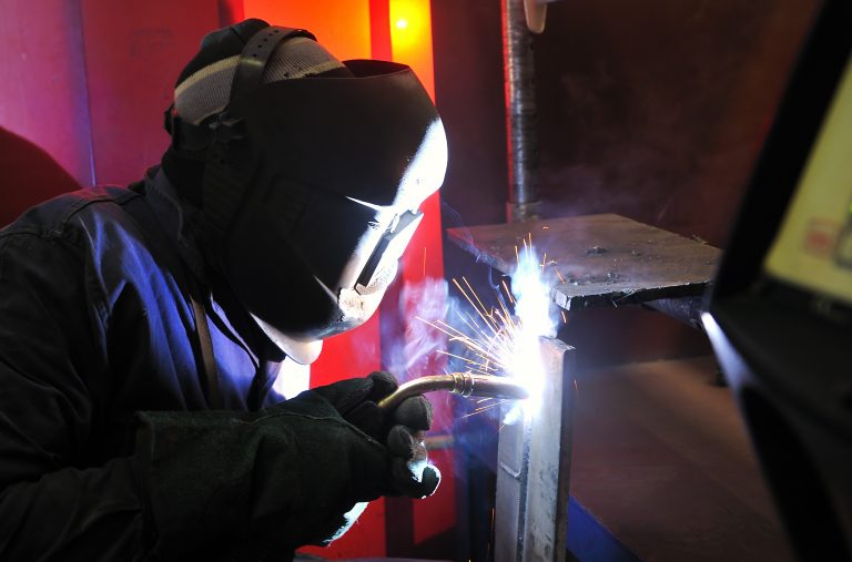 Welder with helmet working on metal piece.