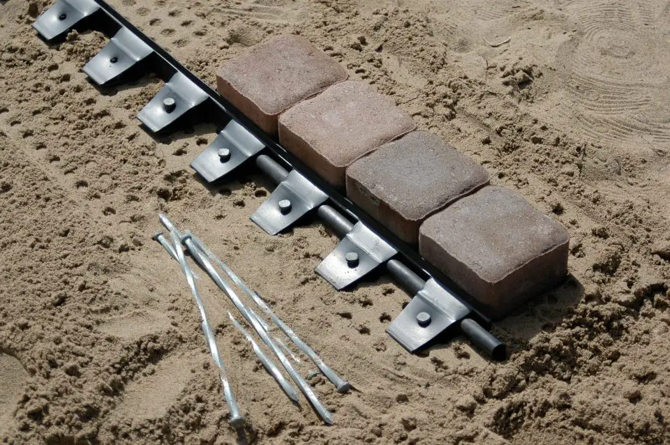 These plastic strips keep bricks contained along the edges of an installation. Backfilled top soil hides the strips when the work is done. The 12″ galvanized spikes hold the support strips in place.