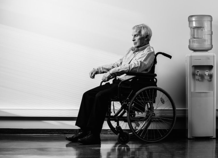 Man in wheelchair beside water cooler indoors.