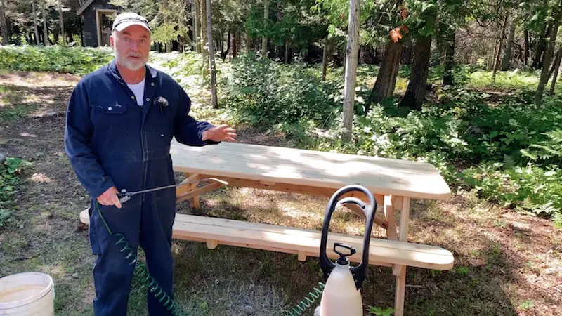 Man applying finish to picnic table outdoors.
