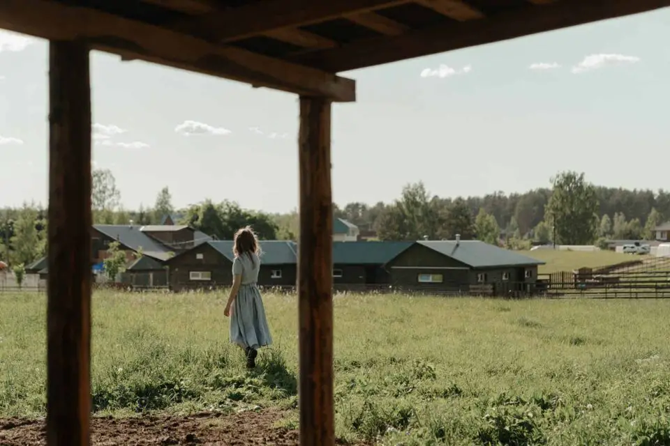 Woman walking in grassy field near rural houses.
