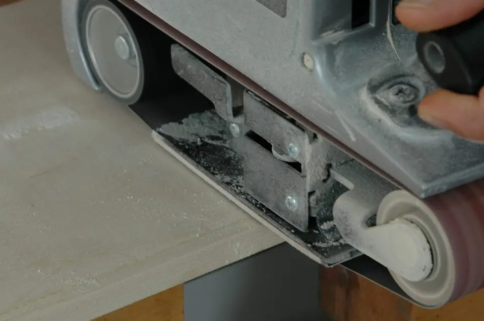 Sanding cross-grain with a belt sander and a 100-grit abrasive to level the edging strip with the plywood. Sanding along the grain is the step that comes next.