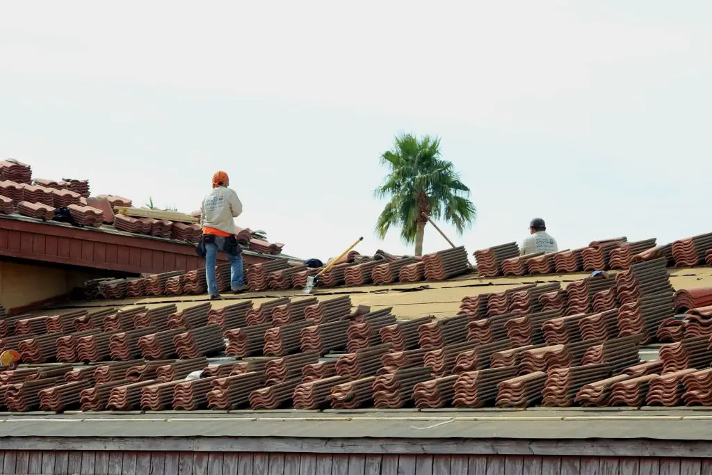 Roofers installing tiles on a house roof.
