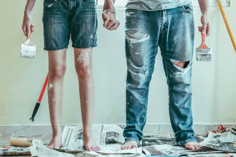 Two people holding paintbrushes, standing on newspapers.