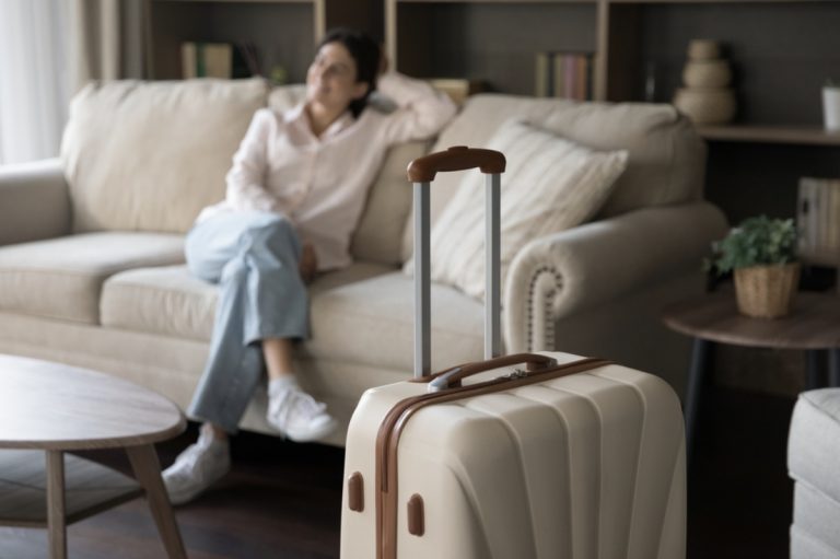 Woman relaxing on couch with suitcase nearby.