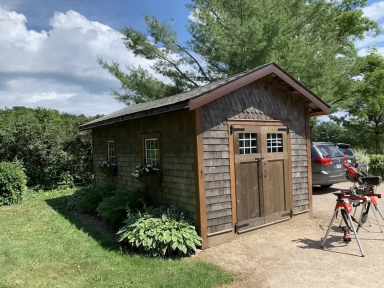 Rustic wooden shed beside parked vehicles and greenery.
