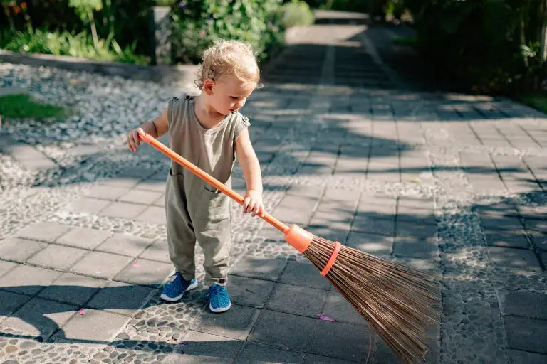 Child sweeping outdoor walkway with a broom