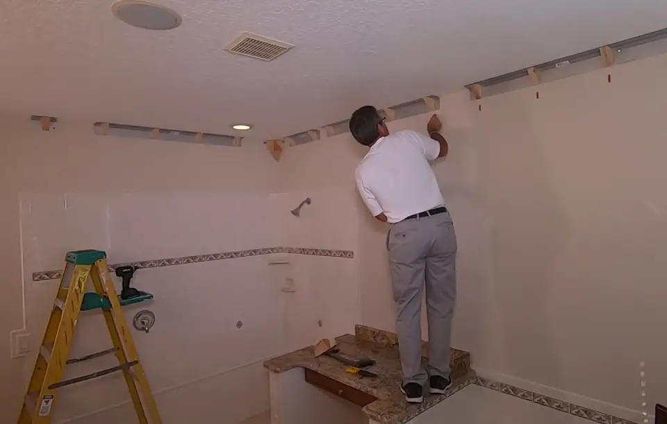 Here Athas Kometas, inventor of EZCrown, installs small, pointed sticky notes to mark where nailing blocks are located on walls. You can’t see these blocks when the crown is up and in place, so you need to mark them.