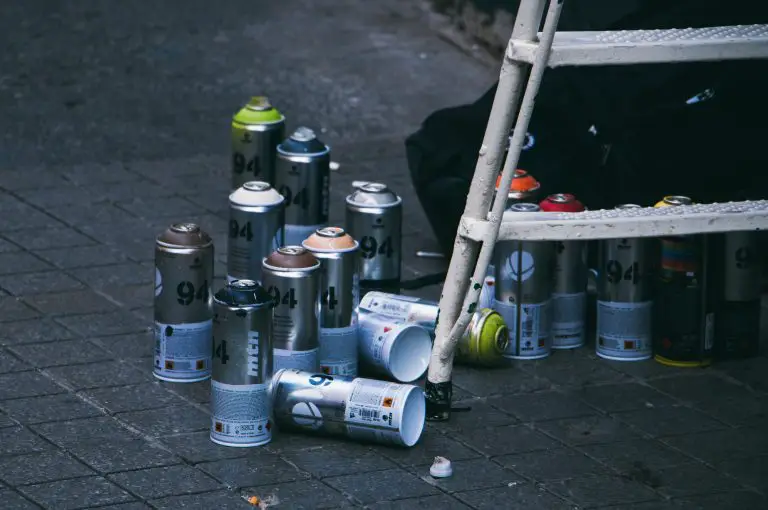 Colourful spray paint cans on sidewalk near ladder.