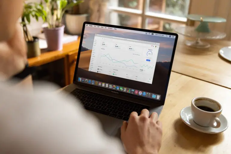 Person analyzing data on laptop with coffee nearby.