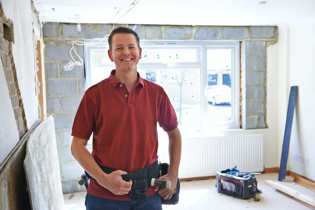 Smiling contractor in unfinished room with tool belt.