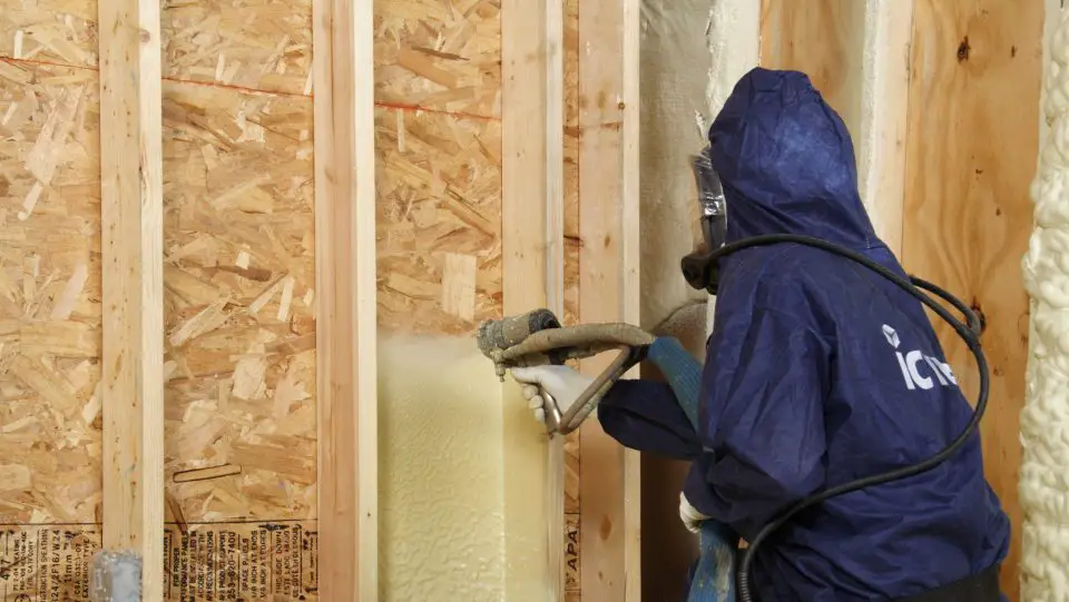 Worker applying spray foam insulation on wood.