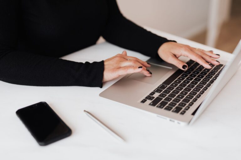 Person typing on laptop with phone nearby.