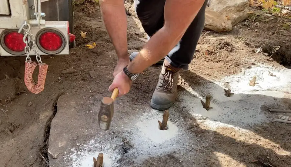 Person using a mallet on metal stakes in dirt.