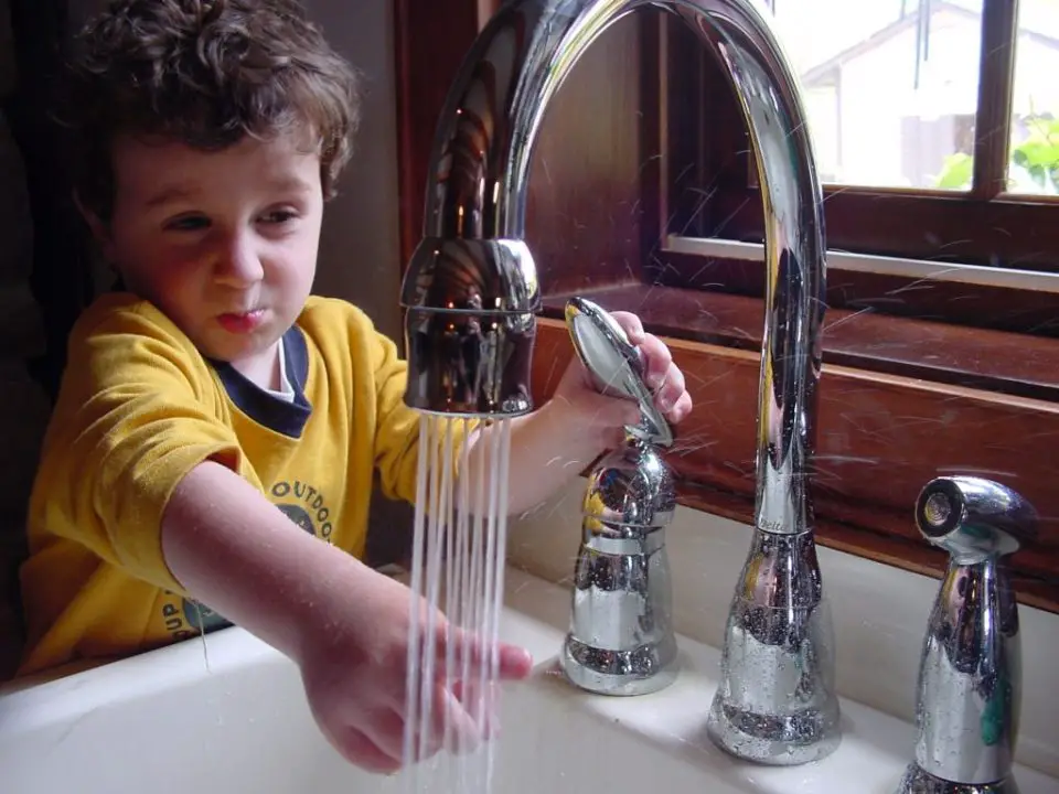Child plays with running faucet water indoors.