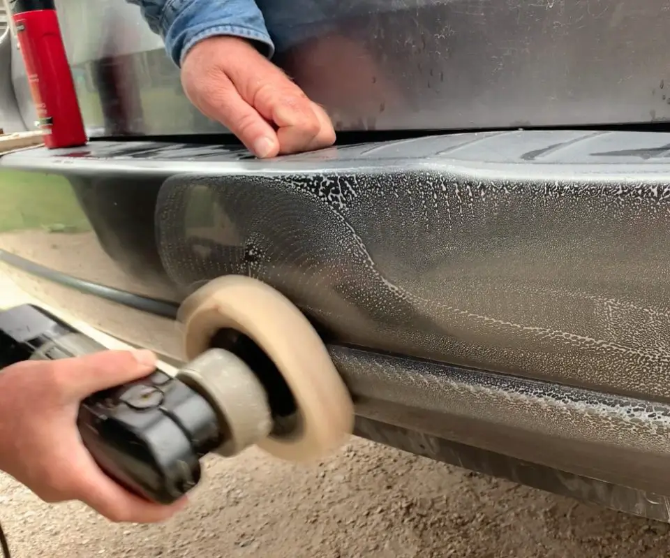 Polishing car bumper with electric buffer tool.