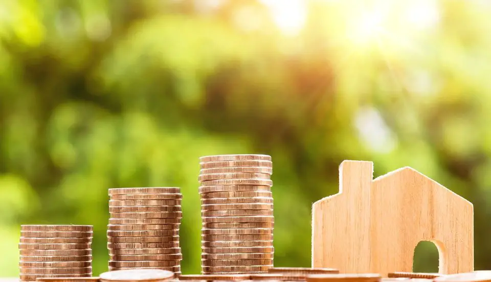 Stacks of coins beside wooden house model