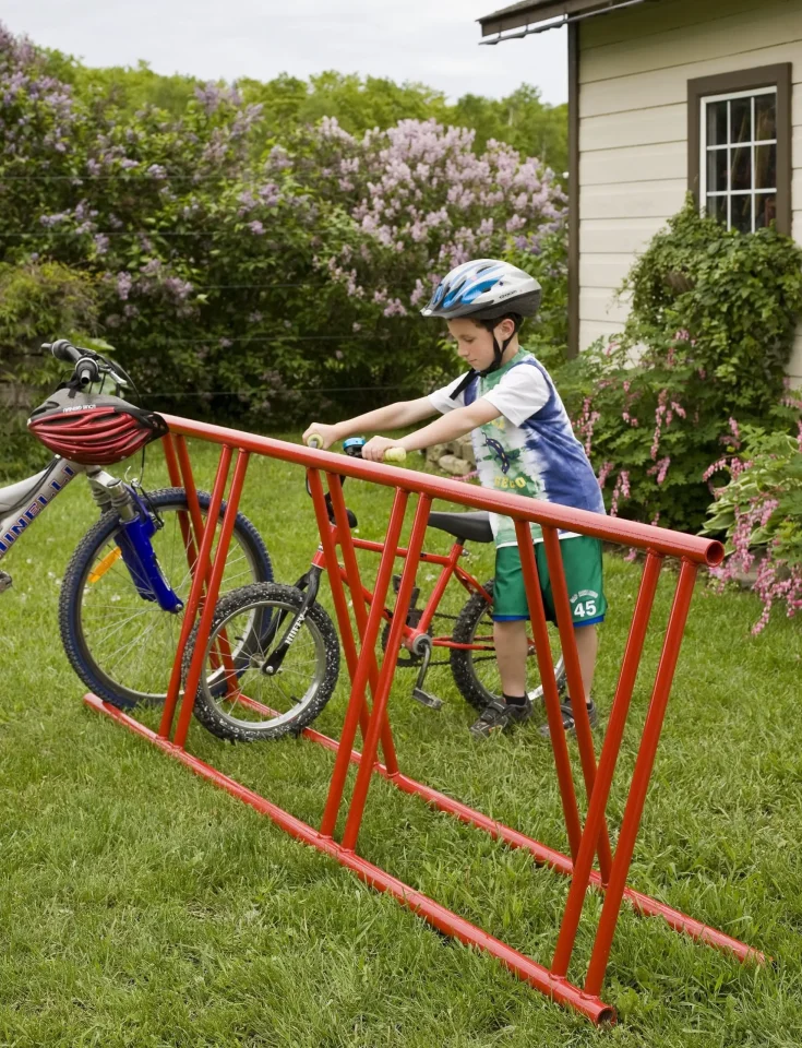 Child in helmet parking bicycle at red rack.