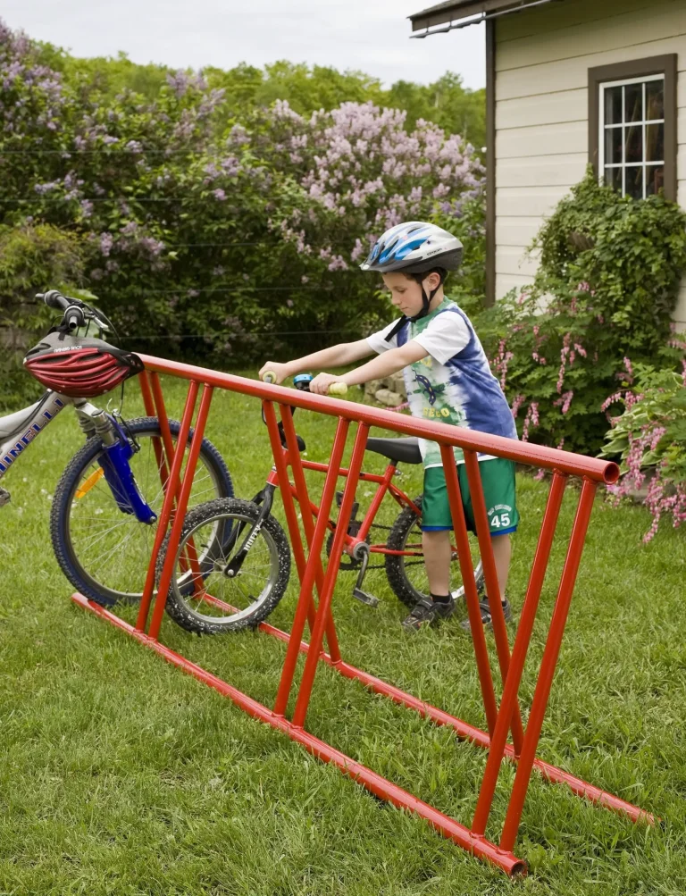 Child in helmet parking bicycle at red rack.