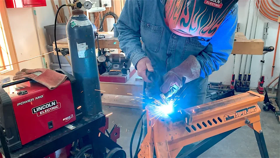 Welder working with protective gear in workshop.