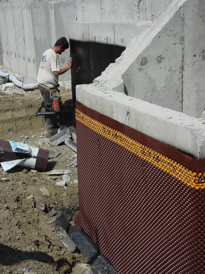 Worker installing waterproofing on concrete foundation wall.