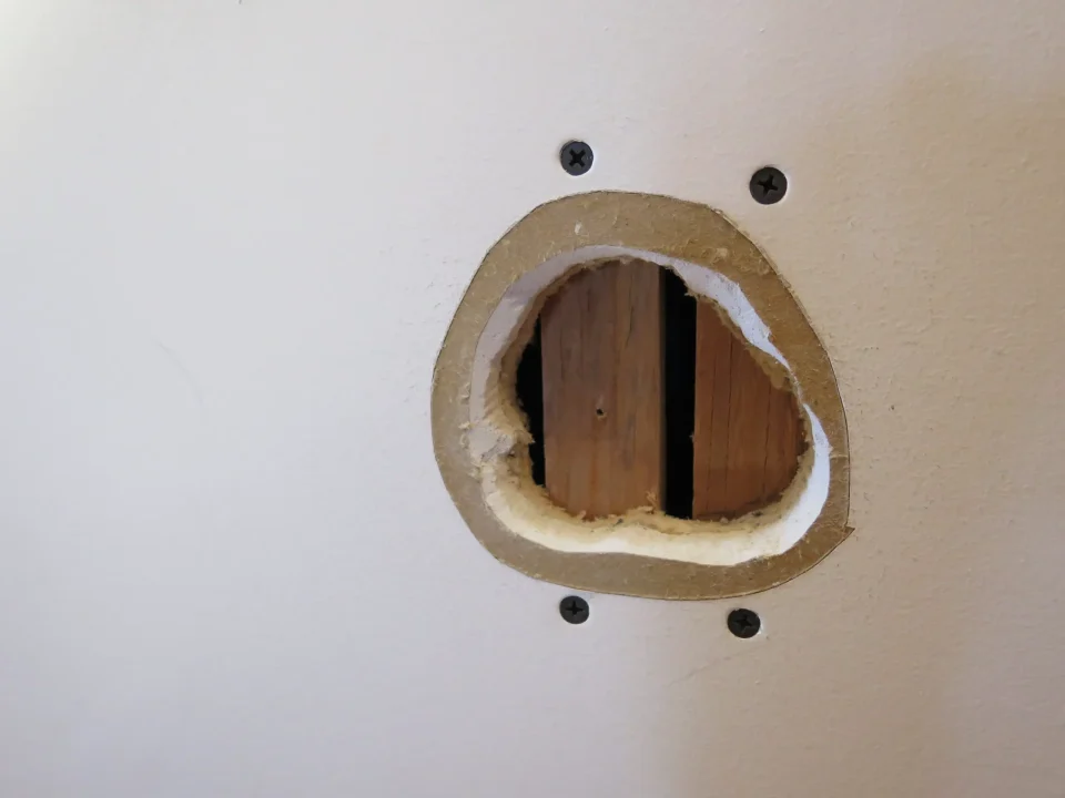 Drywall hole exposing wooden studs on wall.