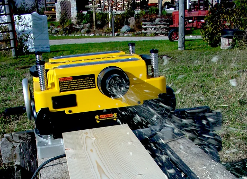 Wood planer smoothing a wooden plank outdoors.