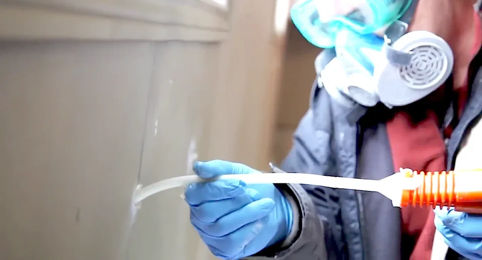 Person applying caulking to wall corner.