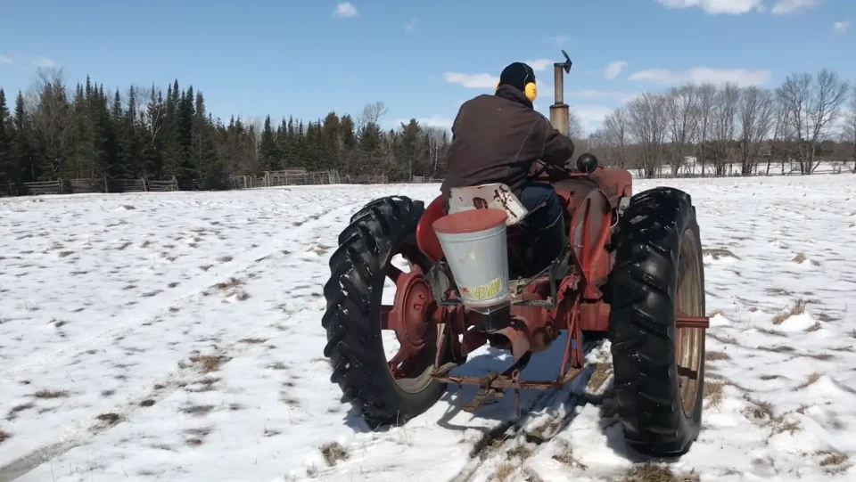 Person drives tractor on snowy field.