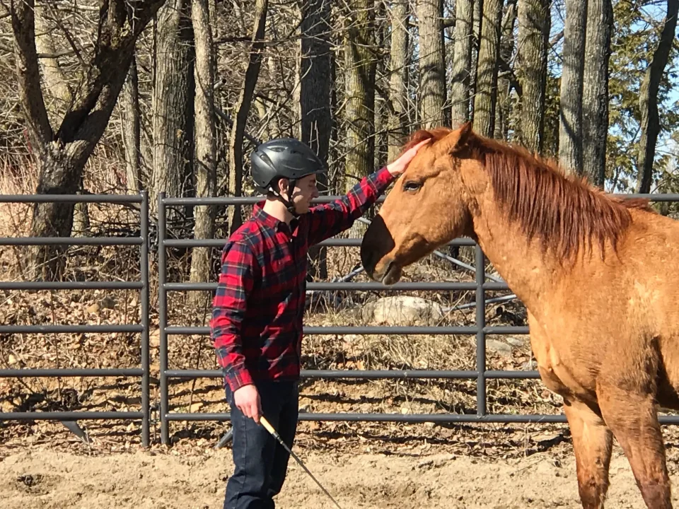 Person petting a horse outdoors, wearing a helmet.